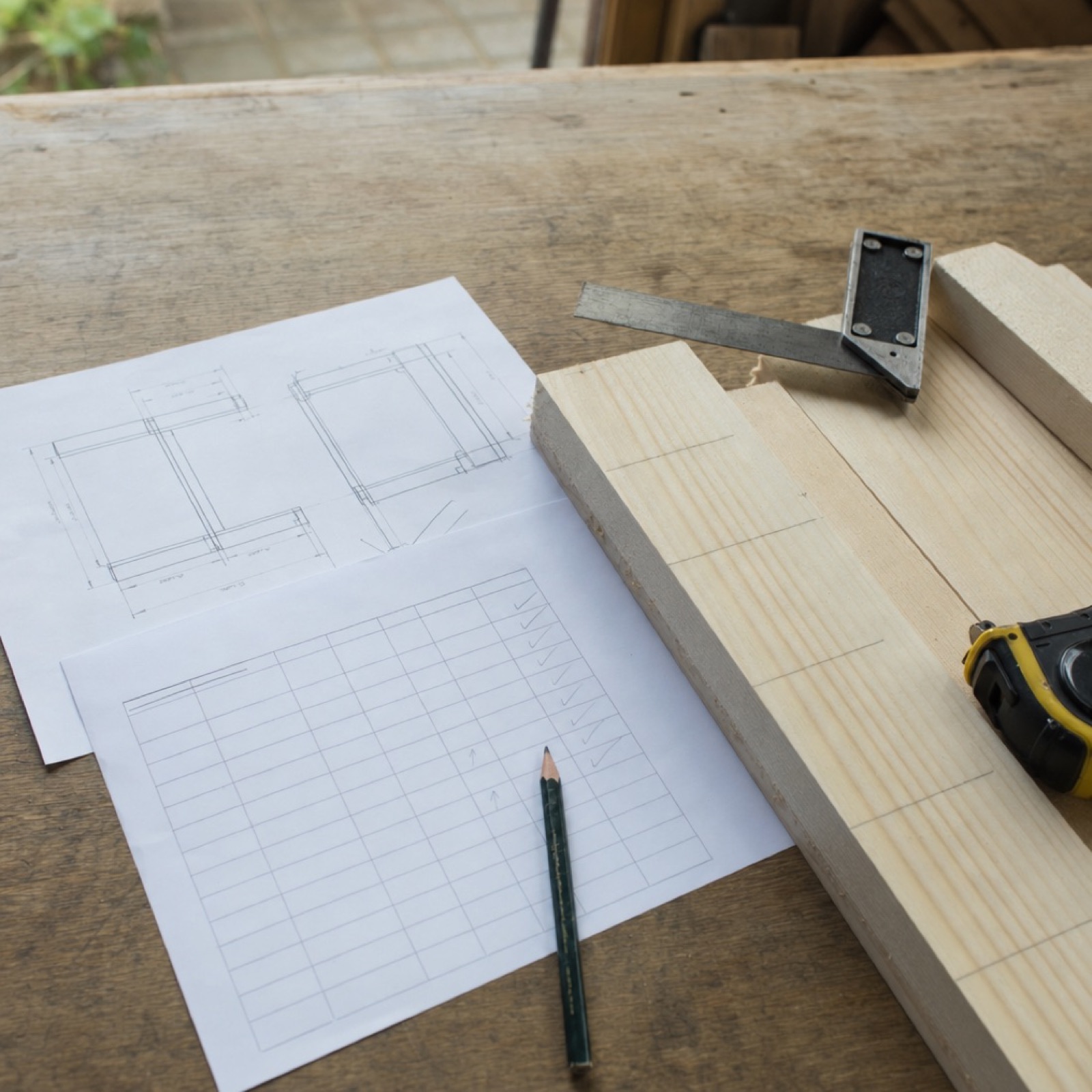 Bouwtekening en materiaallijst op de werkbank naast afgetekende planken